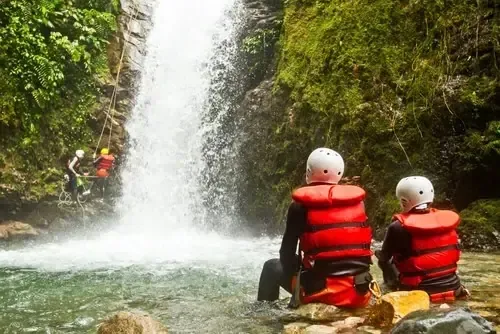 Teilnehmer einer Canyoning-Tour stehen im Bachbett unter einem Wasserfall