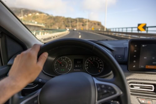 Männliche Hand am Lenkrad mit Blick auf den Tacho der Autos. Verschwommener Blick auf der Frontscheibe auf eine Straße in Madeira.