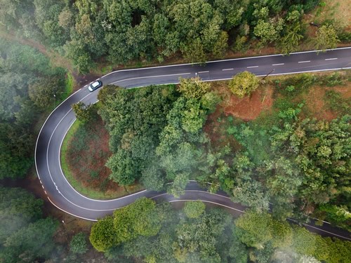 Blick auf eine kurvige Straße aus der Vogelperspektive. Die Straße ist von Bäumen gesäumt und ein Auto fährt darauf entlang.