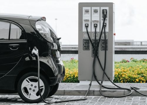 Schwarzer Kleinwagen wird an einer Tanksäule betankt, die Zapfsäule ist eingesteckt.